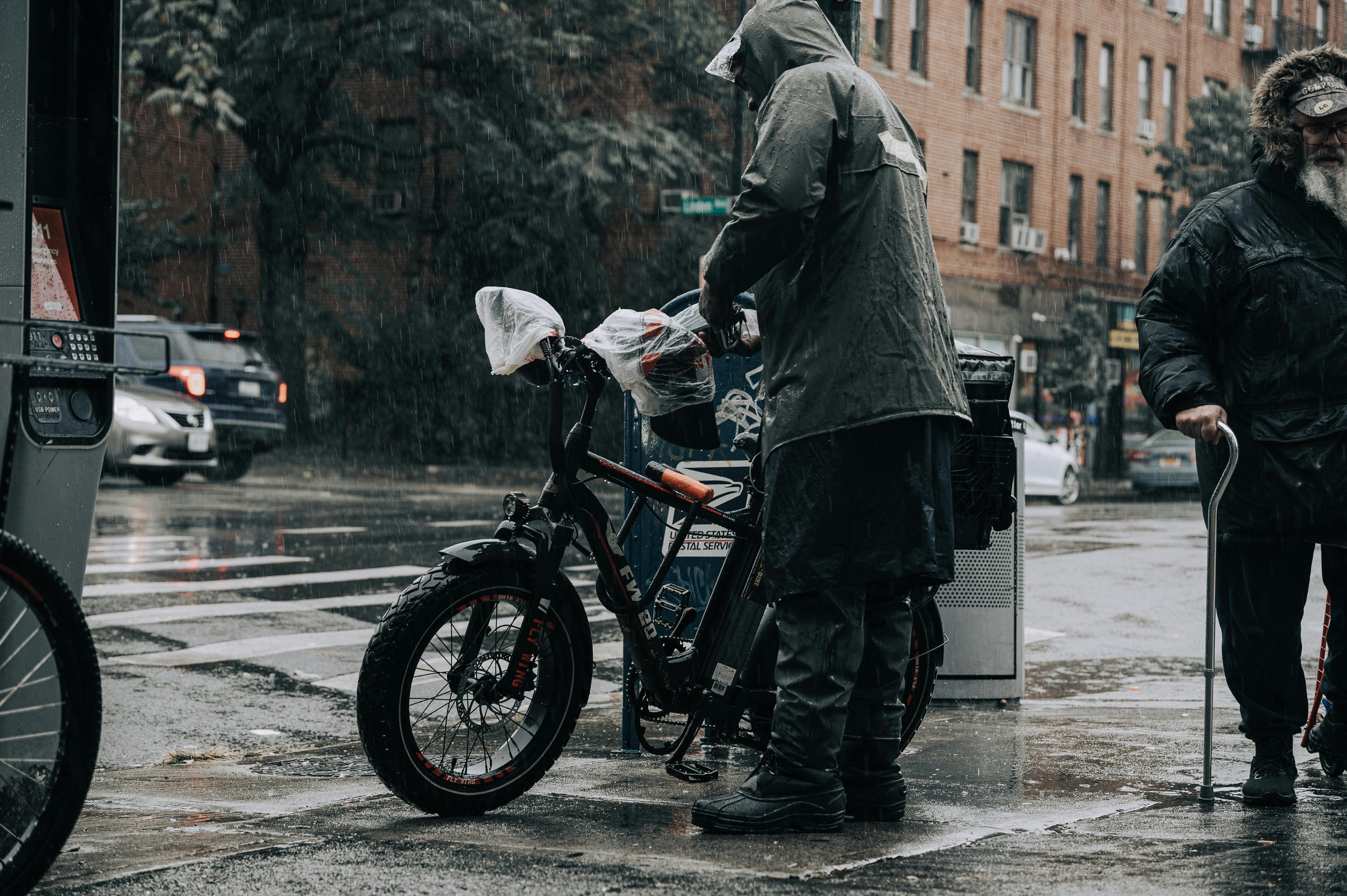 A New York City delivery worker loading an e-bike on a rainy street corner